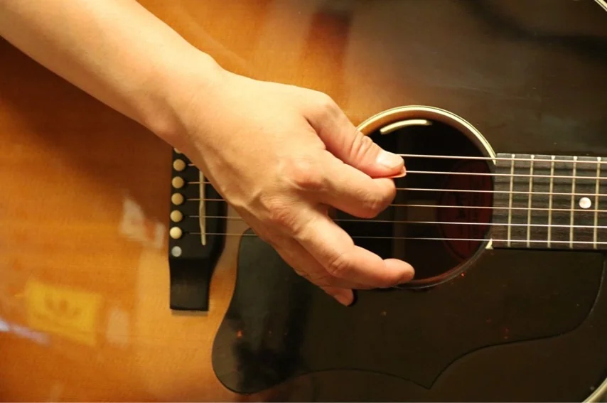 アコースティックギターをピックで演奏しているところ。中指、薬指を開いたオープンスタイル